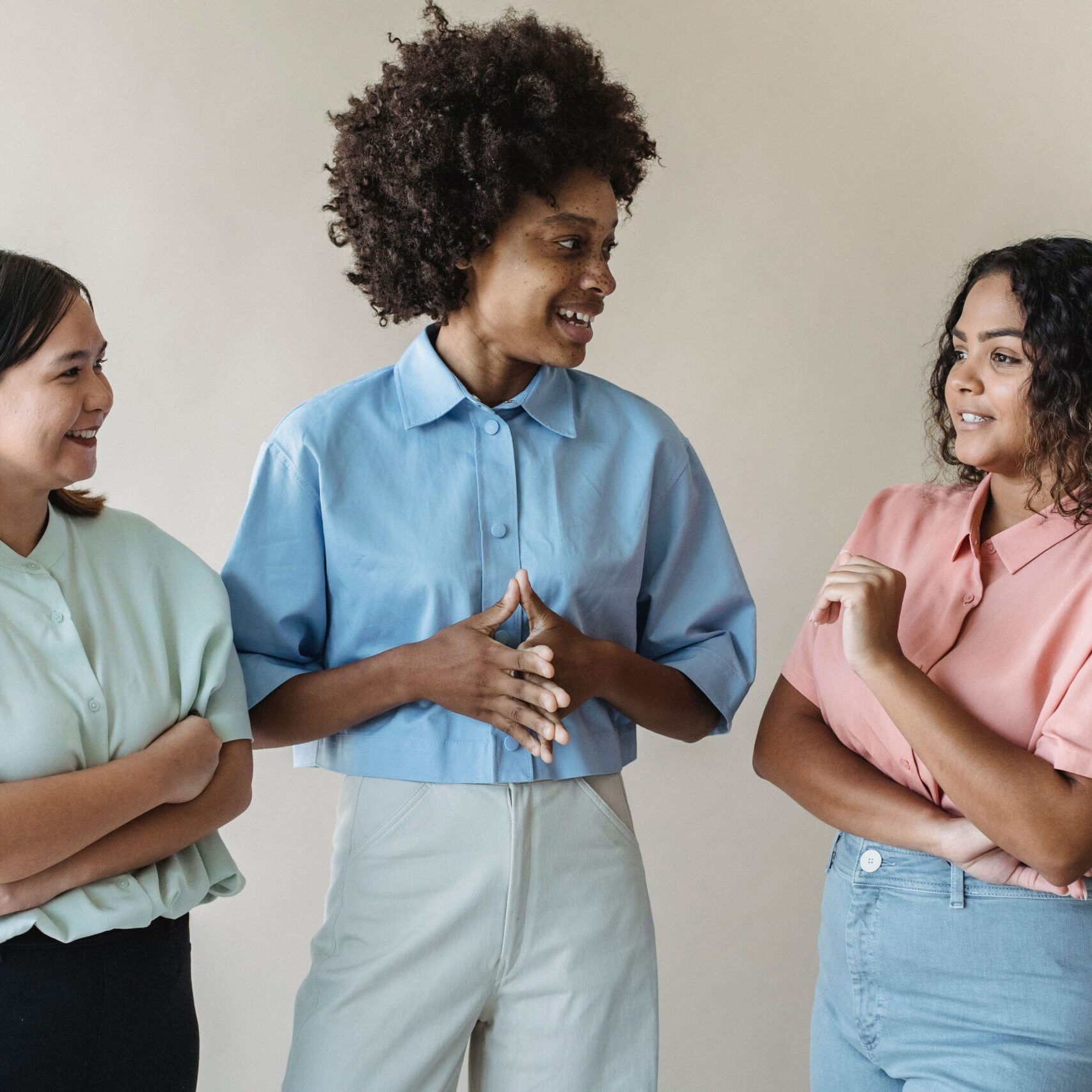 Group of diverse women smiling and talking, showcasing casual fashion in an indoor setting.